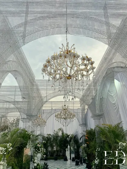 Transforming an open space into a botanical cathedral with grand arches constructed from white wire mesh. Suspended crystal chandeliers add a touch of classic opulence, while thousands of potted plants create a lush, living sanctuary for a truly sustainable luxury wedding.