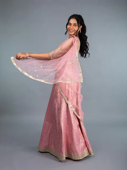 A full view of our stunning pink brocade lehenga. The lightweight fabric and elegant drape make it perfect for twirling on the dance floor at a sangeet or reception. The custom-fit blouse features delicate sleeve detailing, completing this graceful and timeless look.