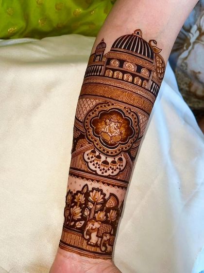 A detailed forearm design featuring a Ganesha motif, elephants, and architectural elements.