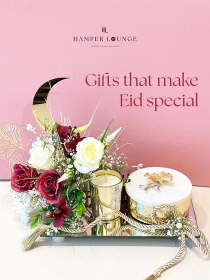 This Eid hamper is all about serene elegance. A mirrored tray holds a scented candle and a box of treats, beautifully arranged with white and red roses and a golden crescent moon accent.