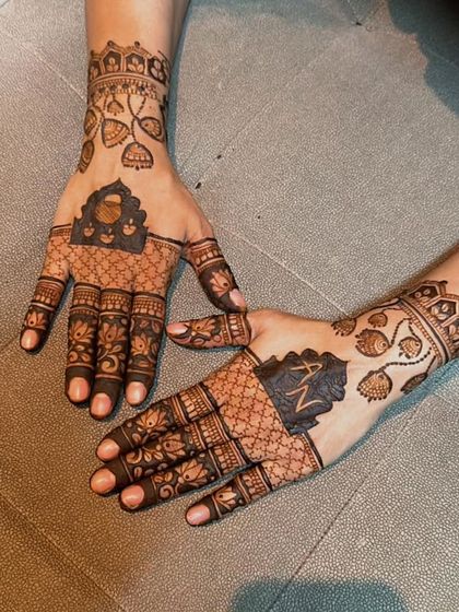 This design combines traditional jharokha windows with personalized initials. The fine net pattern on the fingers and leafy vines on the wrist add to the intricate look, making it special for Karwa Chauth.