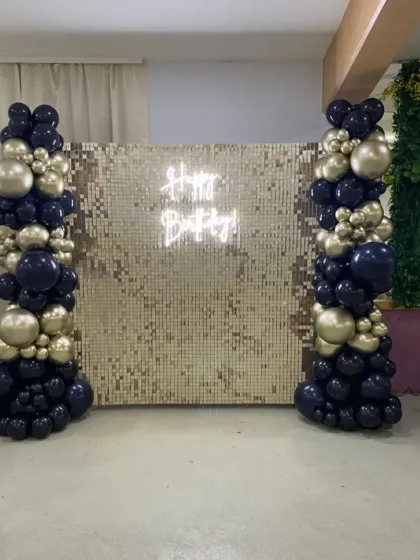 A simple yet elegant setup with a gold sequin wall, a neon sign, and two columns of black and gold balloons.