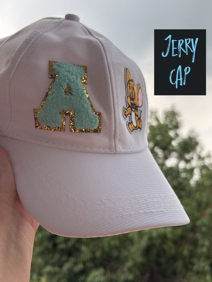 Another angle of the custom 'Jerry Cap', showing the white baseball cap with a personalized initial and character patch. A great example of a unique party favor created at our live station.