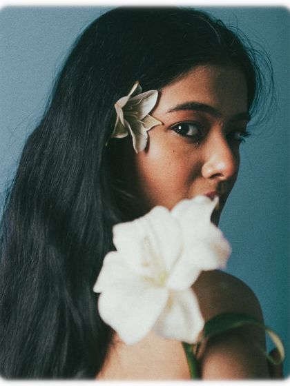 A classic beauty portrait with a twist. The model looks over her shoulder, a white flower in the foreground, creating a lovely composition with layers and depth. Her expression is soft and engaging.