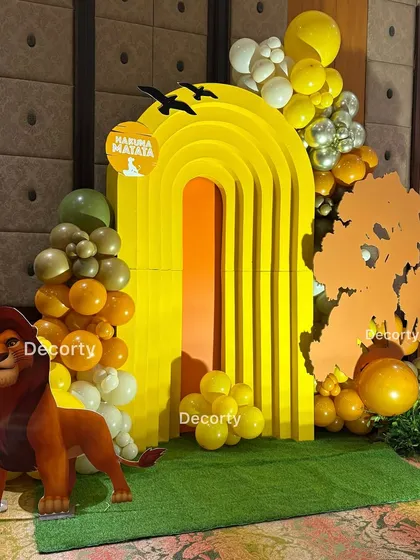 A vibrant photo booth corner with a "Hakuna Matata" sign. The setup includes a life-sized Mufasa cutout and a sunny yellow arch, perfect for capturing memories.