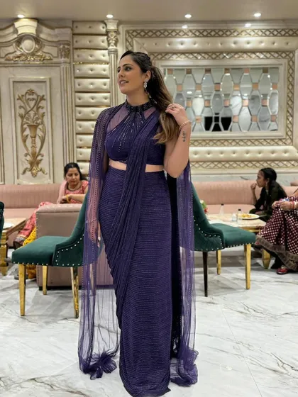Make a statement with this modern purple drape saree. It comes with a stylish high-neck blouse and a flowing cape, giving you an elegant and contemporary look for any cocktail party or reception.