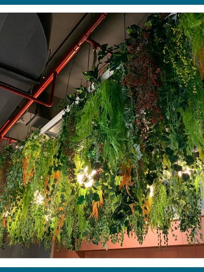 A different angle of a dense artificial hanging installation, with integrated lights peeking through the foliage. This creates a beautiful play of light and shadow, adding depth and a magical quality to the indoor canopy.