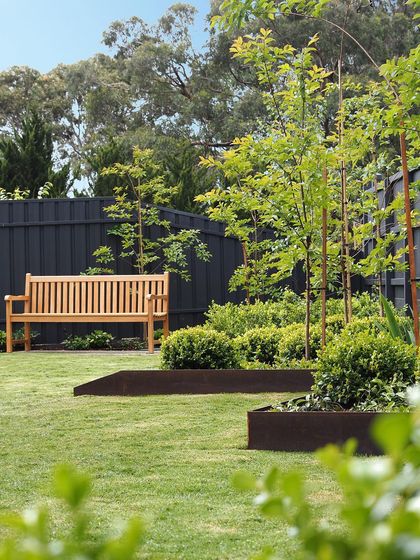 A simple wooden bench provides a quiet spot for contemplation in this modern garden. The design uses raised metal edging for the garden beds to maintain a crisp, clean look.