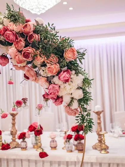 The details matter. This image shows an intricate floral arrangement for a reception table, featuring a beautiful arch of pink and red roses over delicate, individual bud vases, creating a romantic and intimate dining experience.