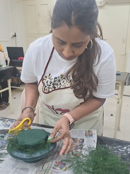Concentration and creativity in action. This student is carefully cutting and placing floral foam, a crucial first step in building a stable and long-lasting arrangement.