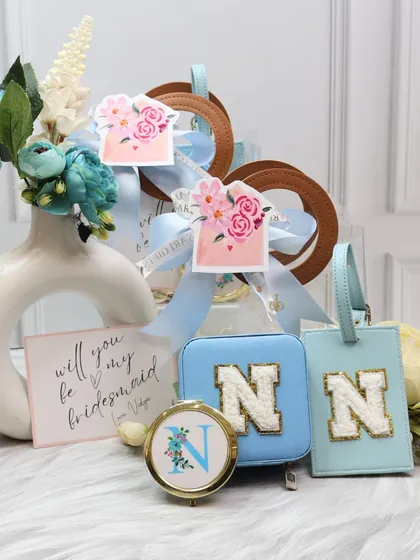 A bridesmaid proposal hamper in a lovely powder blue. The set features a personalized jewelry organizer and luggage tag with chenille patches, along with a custom pocket mirror.