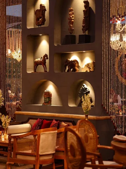 A sophisticated lounge area with a modern-ethnic aesthetic. The built-in wall niches displaying artifacts, combined with comfortable seating and cascading bead curtains, create a stylish and curated space.