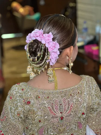 A back view of a detailed bridal bun, featuring a combination of fresh flowers and hanging jhumki-style hair accessories. This is a unique and elegant choice for a wedding ceremony.