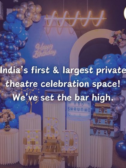 A stylish blue and silver themed birthday decoration. The neon "Happy Birthday" sign, balloon arch, and modern white pedestals create a chic and sophisticated look for any celebration.