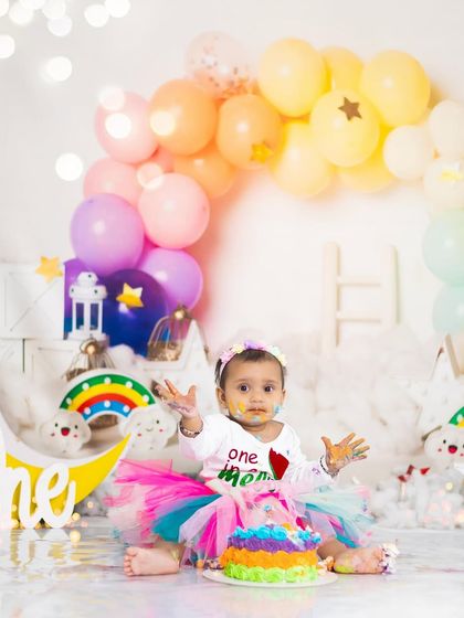 A rainbow-themed cake smash for a colorful first birthday. This setup is complete with a rainbow balloon arch, clouds, and a matching cake.