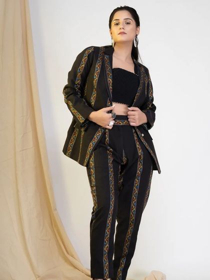 This powerful studio portrait features a black pantsuit with bold, colorful stripes. The model's confident stance and direct gaze make this a striking image for a modern workwear or fashion brand.