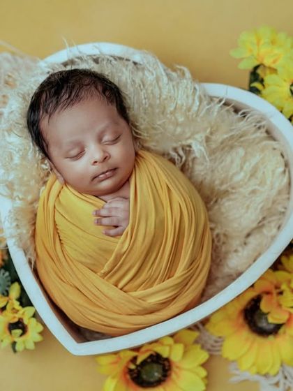 A bundle of sunshine. A bright yellow swaddle brings so much warmth and happiness to this portrait of a sleeping baby in a heart-shaped bowl.