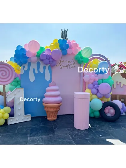 Welcome to a sweet celebration with this vibrant Candyland theme. A giant lollipop, ice cream cone, and colorful balloon arch create a delicious-looking backdrop for a first birthday party.