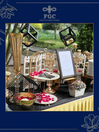 We use decorative elements to enhance our food stations. This setup features geometric birdcages, rose petals, and framed menus to create a whimsical and romantic dessert corner.