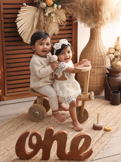 One year old and on the move! This adorable shot of twins on a wooden tricycle is full of playful energy. The "one" sign and boho props create a stylish and memorable first birthday portrait.