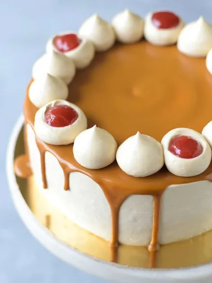A close-up of the Strawberry Biscoff cake, showing the glossy Biscoff drip and the creamy meringue kisses filled with strawberry compote. It's a feast for the eyes and the palate.