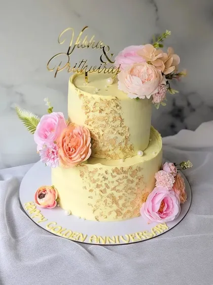 Fifty years of golden moments are celebrated with this two-tier floral cake. A soft yellow buttercream is decorated with gold leaf flakes and arrangements of beautiful pink and peach peonies.