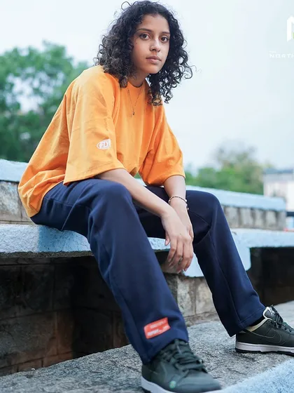 A full shot of the Flypside orange tee, showing its comfortable oversized fit and how it pairs with dark pants for a casual, everyday look.