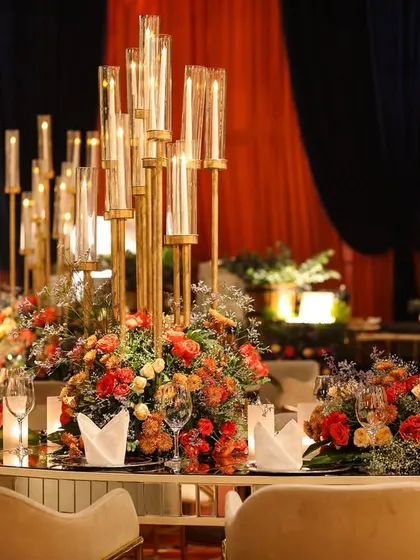 A beautifully set dining table at the gala. The centerpiece is a tall candelabra surrounded by a lush arrangement of orange and red flowers, reflecting the event's color scheme.