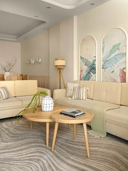 A wider view of the living room, showing the L-shaped sofa and nested coffee tables. The design is rooted in peace, with a soft color palette and an interplay of textures that feels both modern and serene.