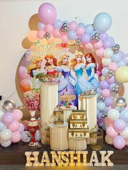 A royal celebration with a Disney Princess theme. This beautiful setup includes a large backdrop with Cinderella, Belle, and Aurora, surrounded by a pastel balloon garland and elegant pedestals for the cake and treats.