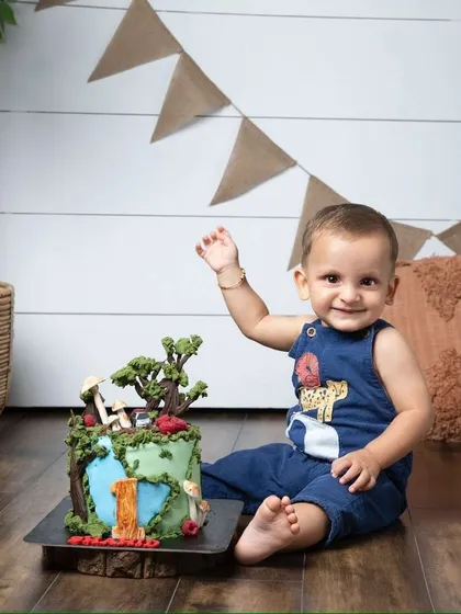 A happy wave next to a beautifully decorated birthday cake. This little boy is ready to celebrate his first birthday in style.