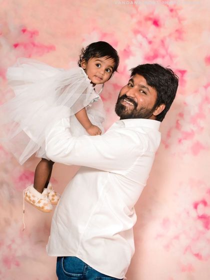 A happy father holds his daughter in a studio setting with a lovely pink floral backdrop. This is a classic father-daughter portrait that is both sweet and timeless.