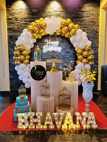 A classic white and gold birthday decor. The balloon ring, neon sign, and plinth arrangement create a timeless and elegant look.