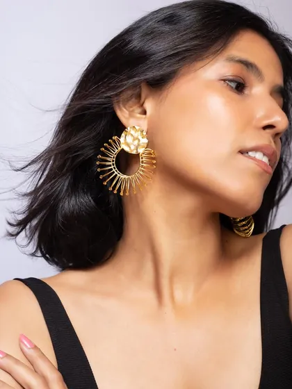 A close-up shot highlighting the unique design of these statement gold earrings. This angle shows the texture and structure of the piece clearly.