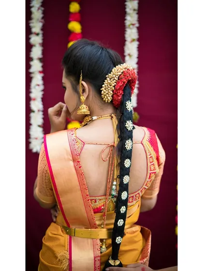 A classic long braid decorated with traditional gold hair accessories ('jadai') and fresh flowers. This style is perfect for muhurtham ceremonies and complements heavy silk sarees.