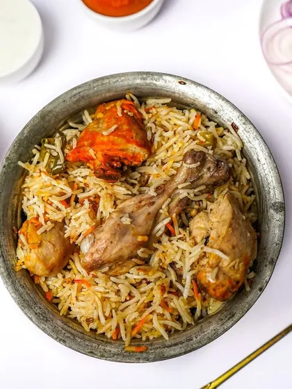 A full handi of chicken biryani with leg pieces and tikka, shot from above with all the classic accompaniments. This comprehensive view is perfect for a menu's main course section.