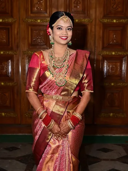 A full-length view of a classic South Indian bride. Her makeup, hair, and traditional red and gold saree come together for a timeless and elegant wedding day look.