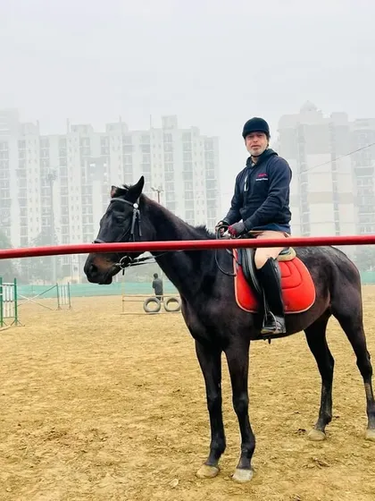 A rider pauses in the arena, with training obstacles and the city buildings in the distance. This demonstrates the authentic equestrian environment we provide.