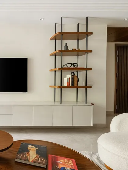 The TV unit combines a sleek white console with a custom open shelving unit. This design provides practical storage while the contrast between the dark metal frame and warm wood shelves adds a modern, graphic element.