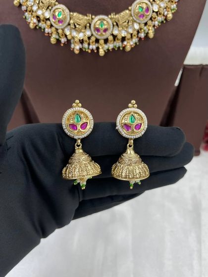 A classic antique gold necklace with circular motifs and multi-colored stones. The set includes matching jhumki earrings, making it a perfect piece for traditional wear.