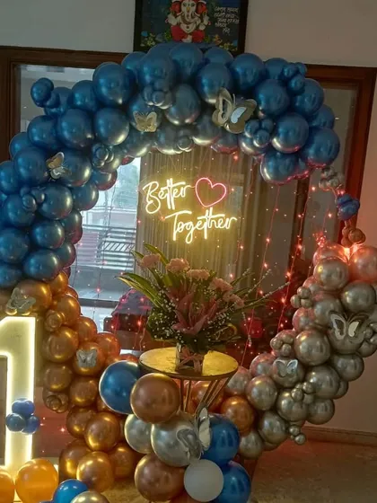 A romantic "Better Together" anniversary setup with a balloon ring in blue, gold, and silver chrome, accented with butterfly details and a light-up number '1'.