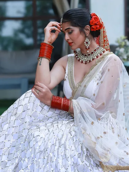 A beautiful and serene bridal portrait. The contrast between the white lehenga and the traditional red jewelry and flowers is timeless and elegant.