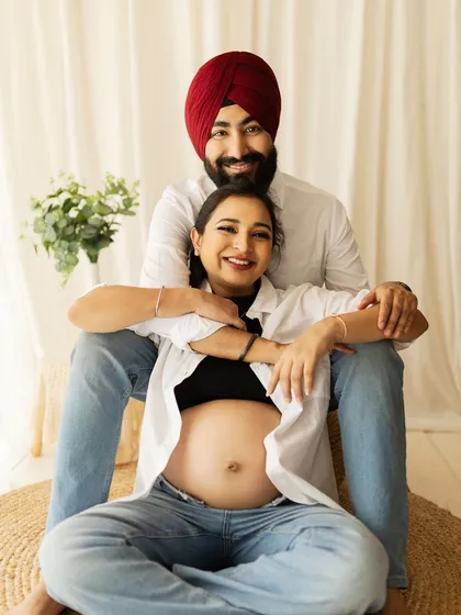 A happy couple in a casual, light-filled setting. The simple white shirts and jeans, paired with the natural decor, create a relaxed and authentic maternity portrait.