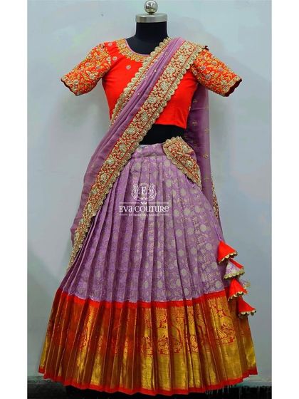 A half-saree lehenga for older girls. This features a lavender Banarasi skirt with a red and gold border, a bright orange embroidered blouse, and a lavender dupatta with a heavy work border.