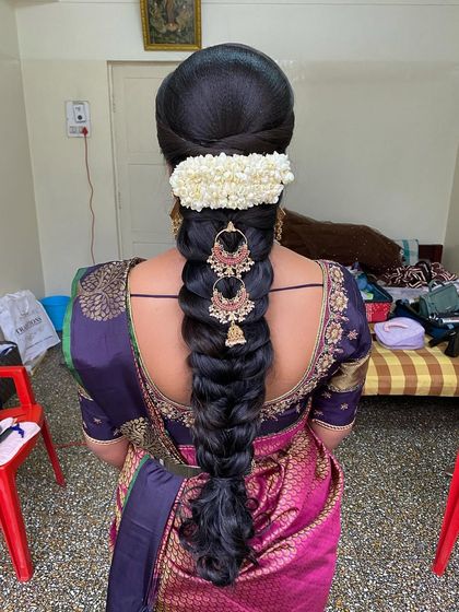 A stunning Varpooja look featuring a thick braid, a jasmine gajra, and elegant gold jhumka-style hair accessories that hang beautifully along the plait.