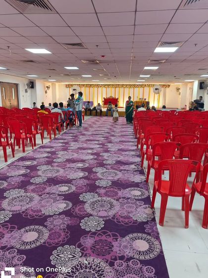 A birthday event hall with a purple floral carpet and red plastic chairs. I can provide different types of carpets and seating to fit your budget and theme.