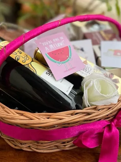 Another view of our colorful anniversary basket, showcasing the bright pink handle and ribbon. This gift combines celebration with sweetness, featuring wine, chocolates, and fun greeting cards.