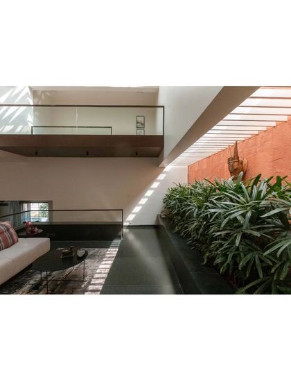In this living area of the Notan Home, a long planter of indoor greenery runs alongside the seating. The terracotta-colored wall and the play of light from above create a warm, nature-inspired atmosphere.