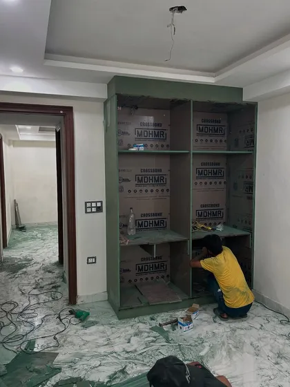 We use high-quality, moisture-resistant green plywood for wardrobes and kitchens to ensure longevity. Here, a carpenter is assembling the frame of a large bedroom wardrobe.