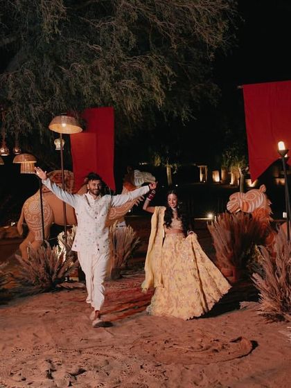 The couple making their grand entrance at the Mehendi sundowner, walking through a path lit by torches against the desert landscape.